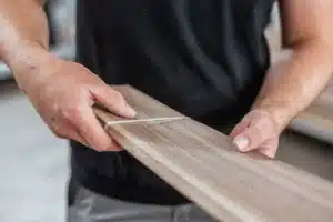 First Class MasterCraft team member holding a custom-cut wood strip—preparing materials for handcrafted furniture frame in Fort Lee workshop
